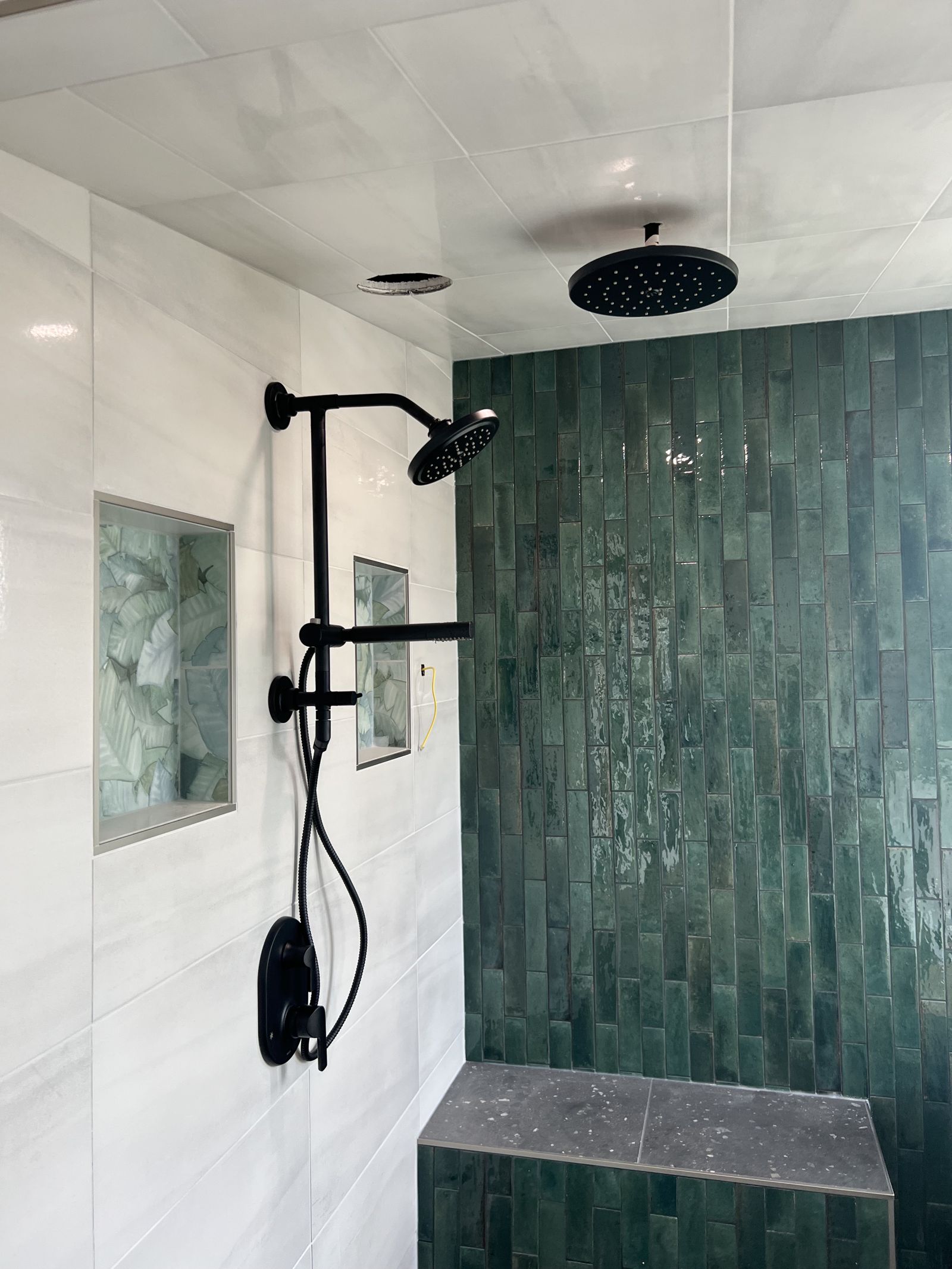 Walk-in shower with green glazed tile feature wall and matte black rain shower